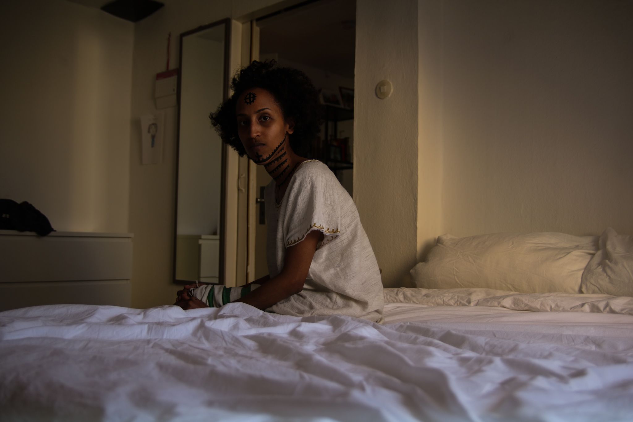 zu sehen. Ihr Kopf ist nach links hinter sich gedreht. Sie blickt direkt in die Kamera. Ihr Hals und ihre Stirn sind mit traditionellen äthiopischen Tätowierungen bemalt.